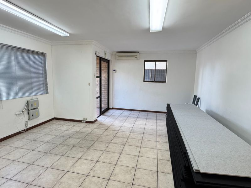 A clean, open-plan office space featuring ceramic tile flooring, fluorescent lighting, and a wall-mounted air conditioning unit.