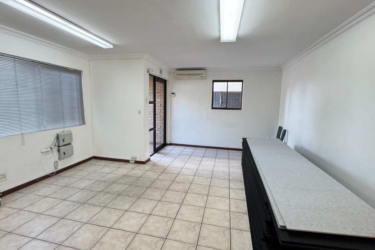 A clean, open-plan office space featuring ceramic tile flooring, fluorescent lighting, and a wall-mounted air conditioning unit.