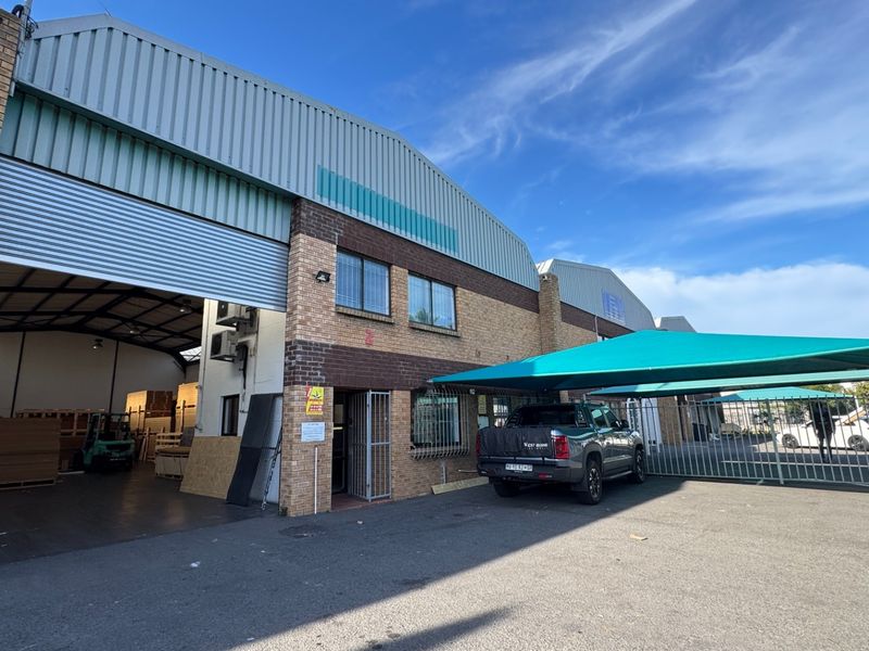 Industrial property exterior featuring a large roller shutter door, brick facade, and a covered parking area with shade cloth.