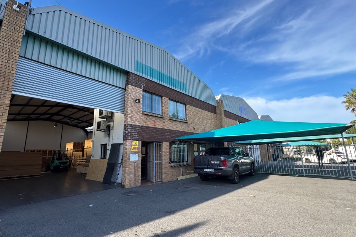 Industrial property exterior featuring a large roller shutter door, brick facade, and a covered parking area with shade cloth.