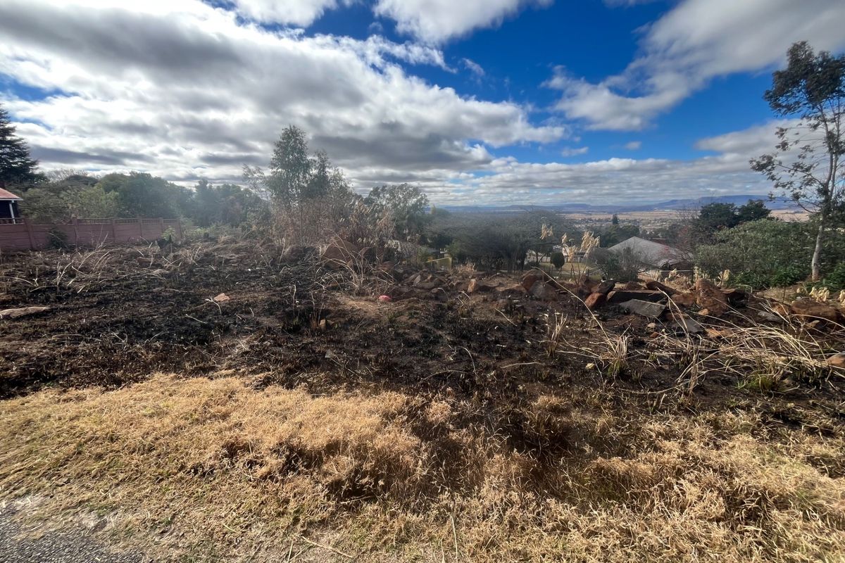 A wide-angle view of a vacant residential plot featuring natural rock formations and landscape with signs of recent fire damage to the vegetation.