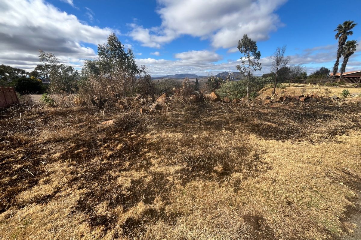 A view of a vacant residential plot featuring natural rock formations, indigenous trees, and signs of recent fire damage to the ground cover.