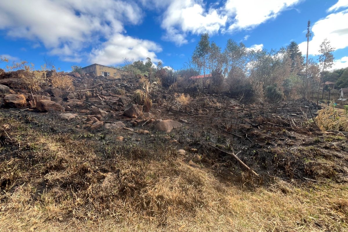 A sloped residential plot featuring rocky terrain and signs of recent fire damage to the vegetation.
