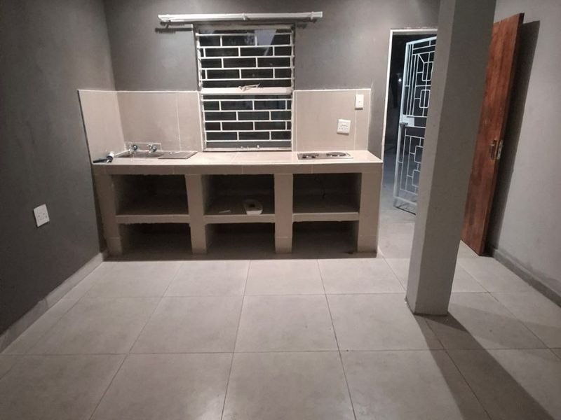 A basic, empty kitchen featuring a built-in concrete counter with a sink and hob, tiled flooring, and a structural support column.