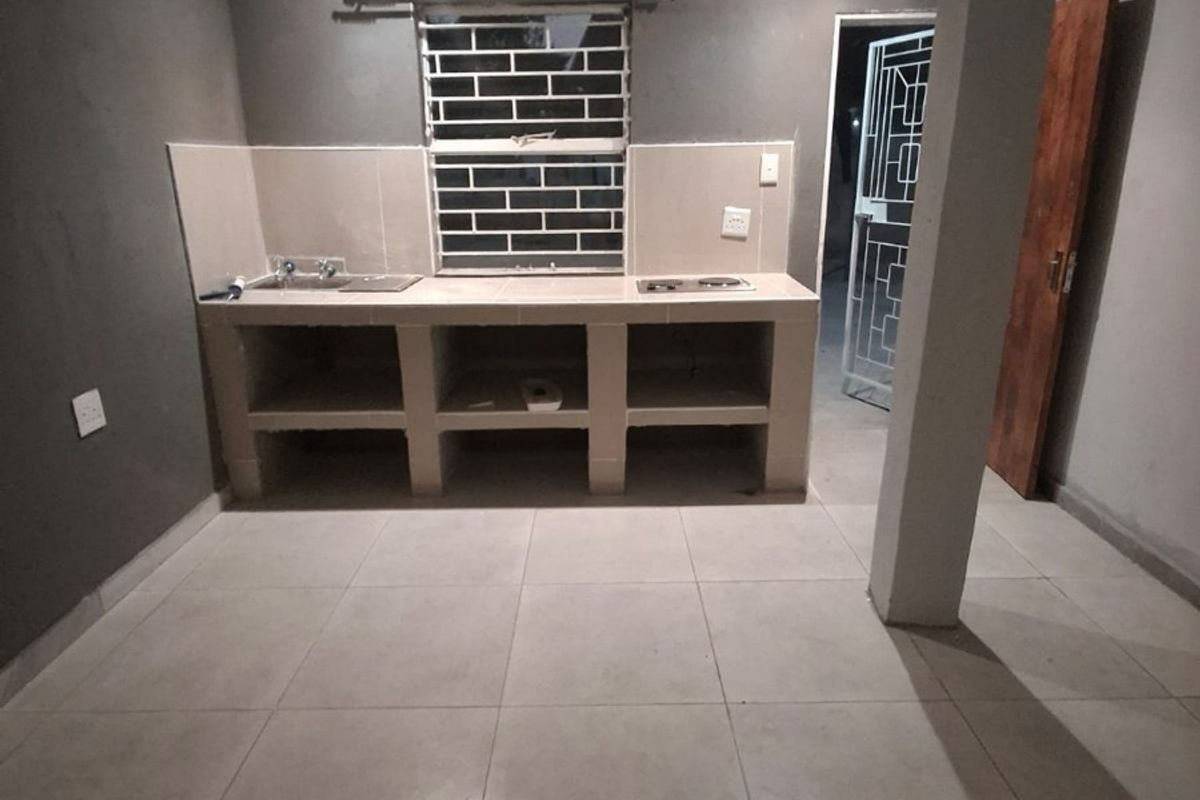 A basic, empty kitchen featuring a built-in concrete counter with a sink and hob, tiled flooring, and a structural support column.