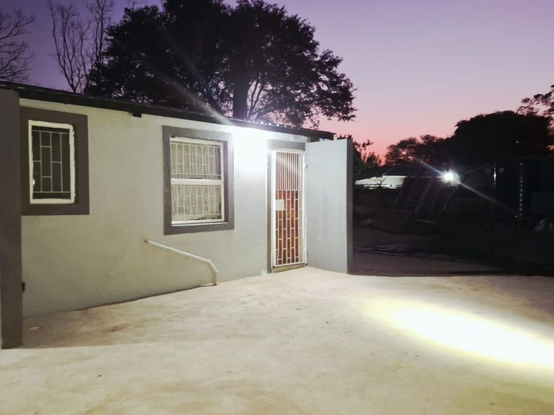 Exterior view of the rear building facade featuring security bars on windows and a concrete patio area at dusk.