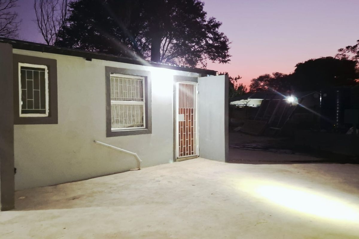Exterior view of the rear building facade featuring security bars on windows and a concrete patio area at dusk.