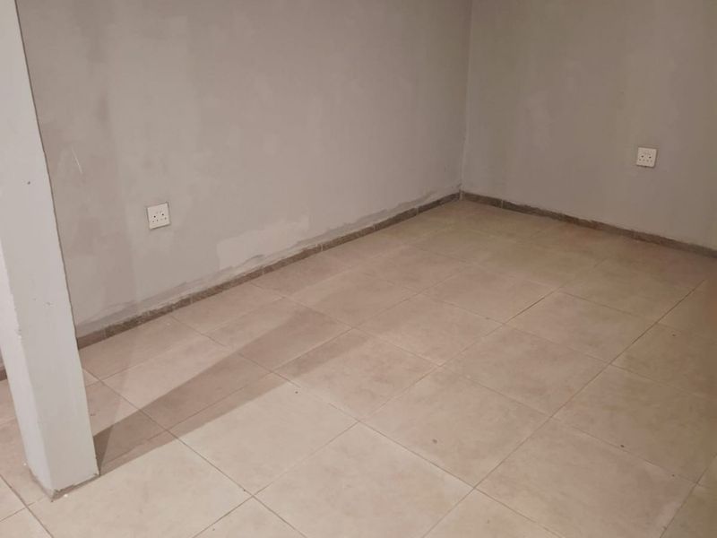 An empty, unfinished bedroom featuring neutral ceramic floor tiles and basic electrical fixtures, ready for final painting and interior design.