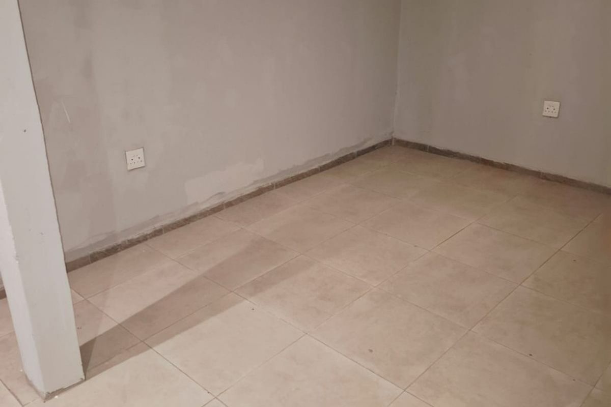 An empty, unfinished bedroom featuring neutral ceramic floor tiles and basic electrical fixtures, ready for final painting and interior design.