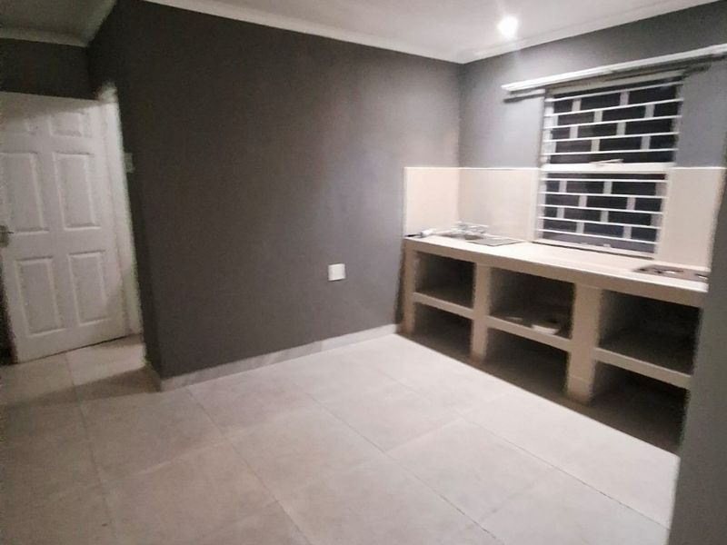 A basic, empty kitchen area featuring a concrete counter, stainless steel sink, tiled flooring, and security bars on the window.