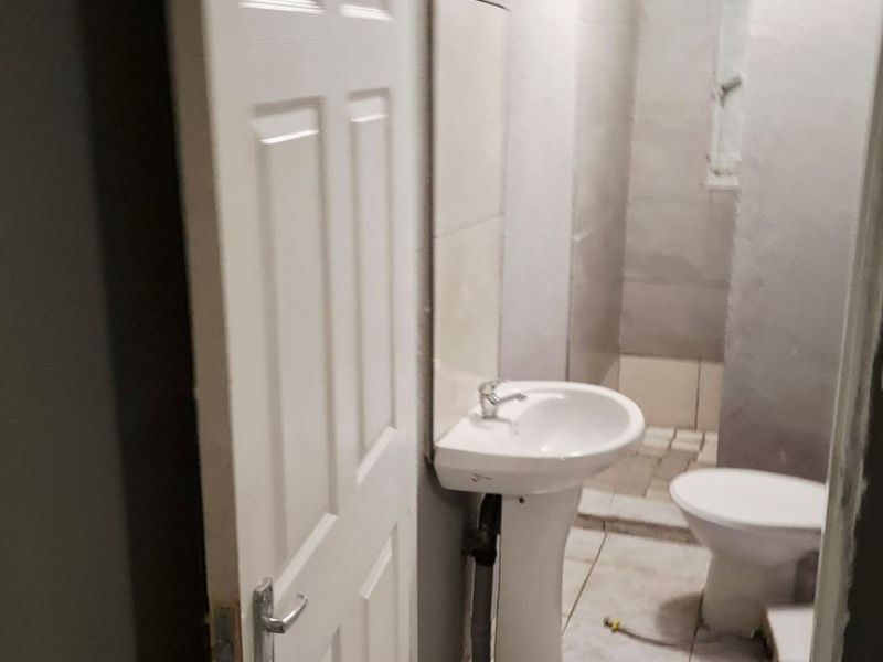 A small, functional bathroom featuring a pedestal basin and toilet with tiled finishes, currently requiring cosmetic updates and finishing touches.