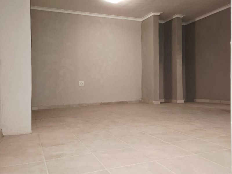 An empty, neutrally painted living area featuring ceramic floor tiles and coved cornicing, ready for interior design and furnishing.