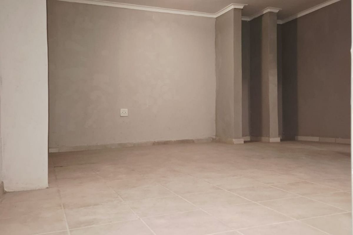 An empty, neutrally painted living area featuring ceramic floor tiles and coved cornicing, ready for interior design and furnishing.