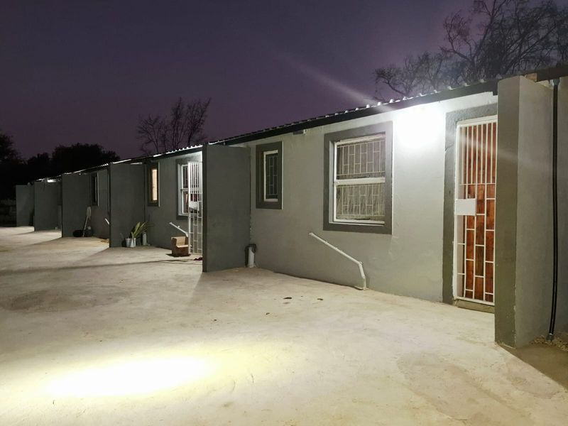 Night view of a row of residential units featuring concrete driveway access, security gates, and exterior wall lighting.