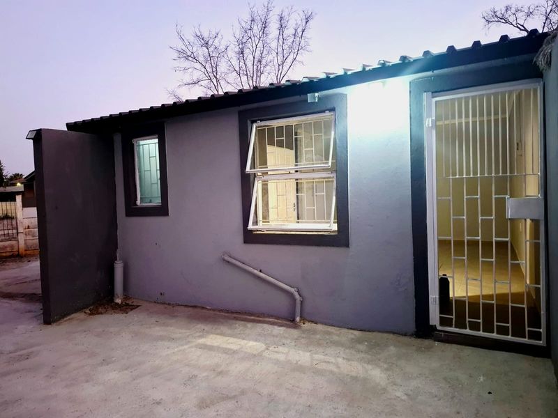 Rear exterior view of the property featuring a concrete patio, security gate, and security bars on the windows.