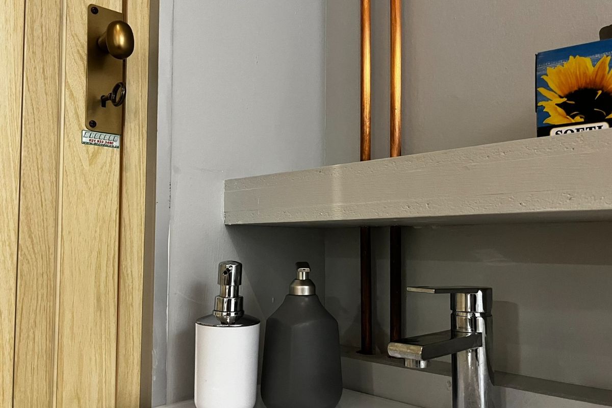 Close-up view of a bathroom vanity area featuring a modern basin mixer tap, exposed copper piping, and a floating shelf.