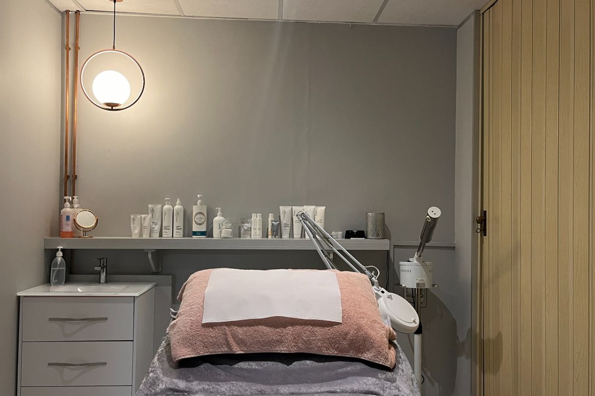 A functional treatment room featuring a built-in vanity with sink, wall-mounted shelving, and modern pendant lighting, suitable for professional beauty or clinical services.