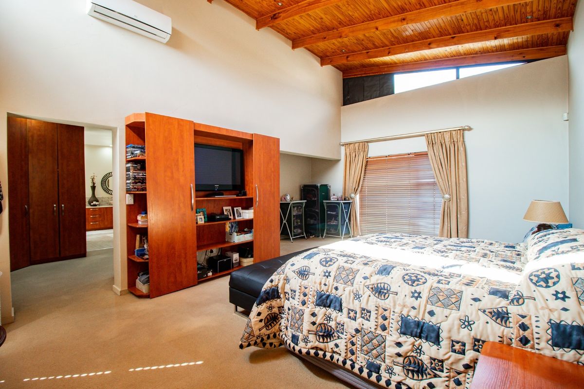 Spacious bedroom featuring a high exposed timber ceiling, split-system air conditioning, and an adjoining en-suite bathroom area.
