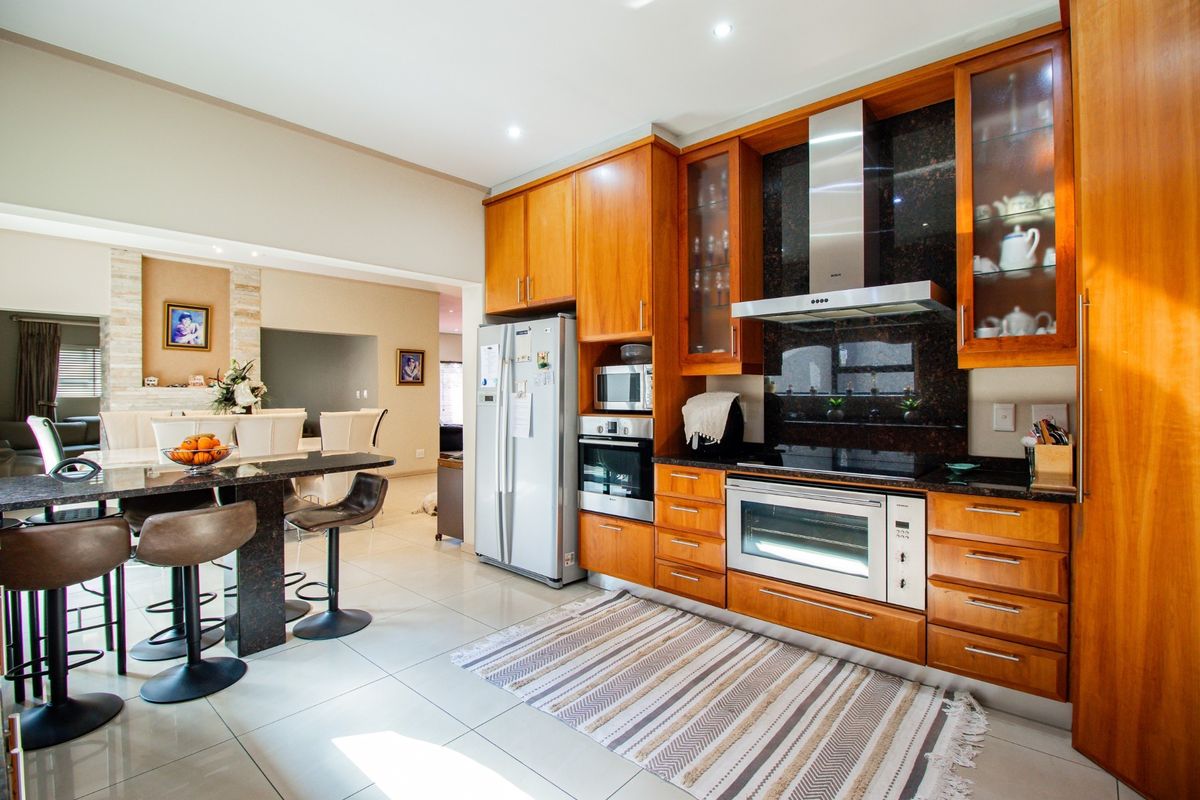 Modern kitchen featuring warm wooden cabinetry, granite countertops, integrated appliances, and a breakfast bar, seamlessly flowing into the adjacent living area.