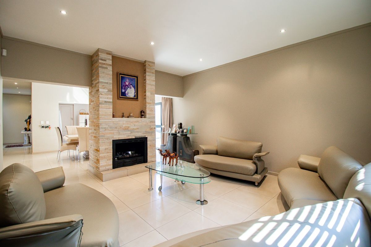 Spacious living room featuring a central stone-clad fireplace, neutral wall tones, and polished porcelain floor tiles with recessed lighting.