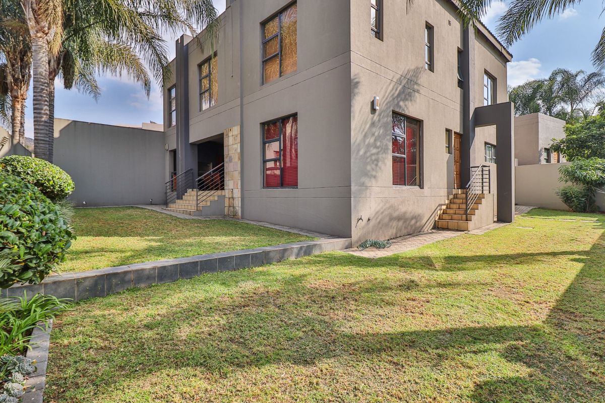 Rear view of a modern two-story house featuring grey rendered walls, stone accents, and a well-maintained garden with paved steps and metal railings.