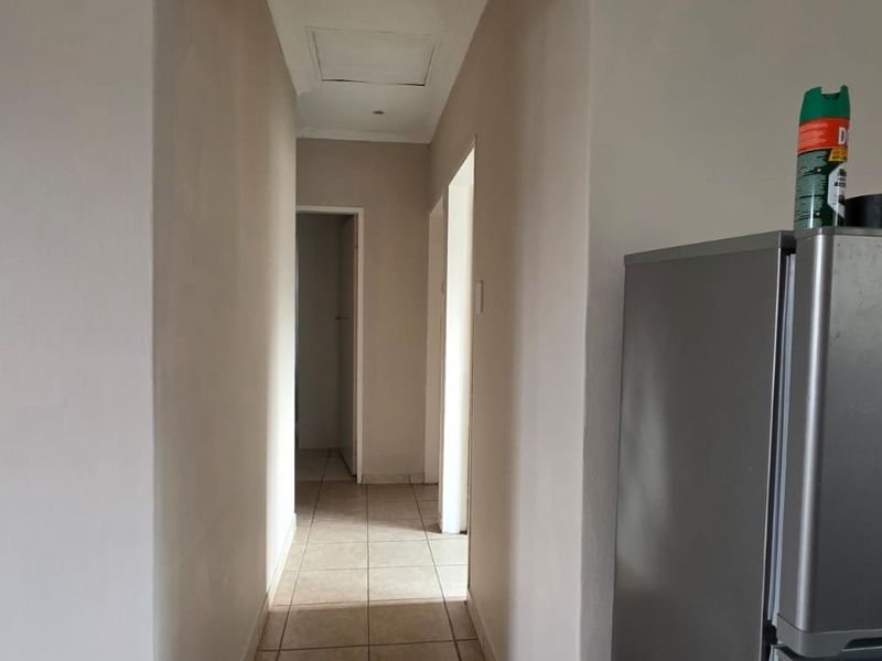 A simple, neutral-toned hallway featuring tiled flooring and a ceiling access hatch, providing access to other areas of the home.