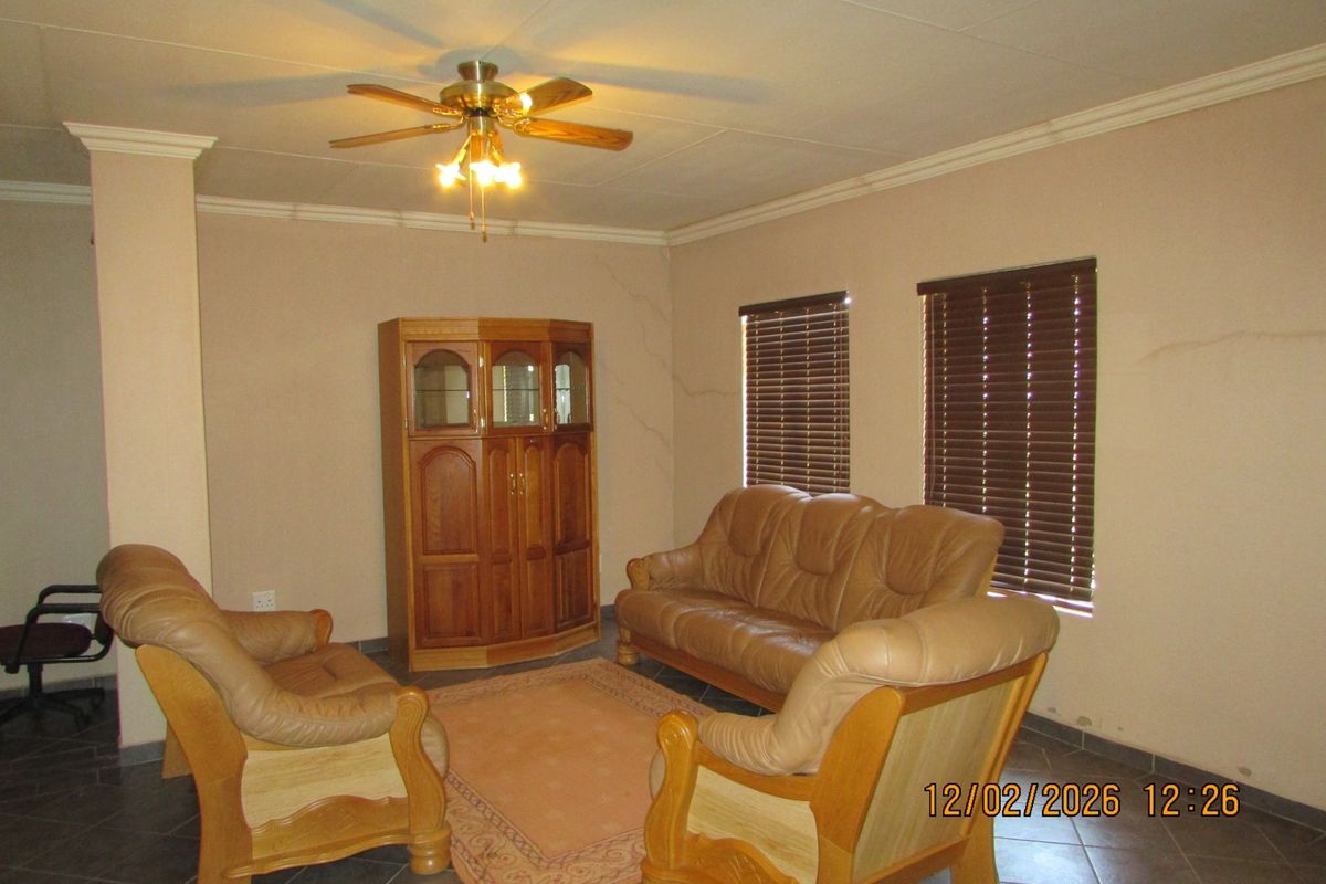 A living room featuring tiled flooring, a ceiling fan, and venetian blinds, showing visible wall cracks requiring maintenance.