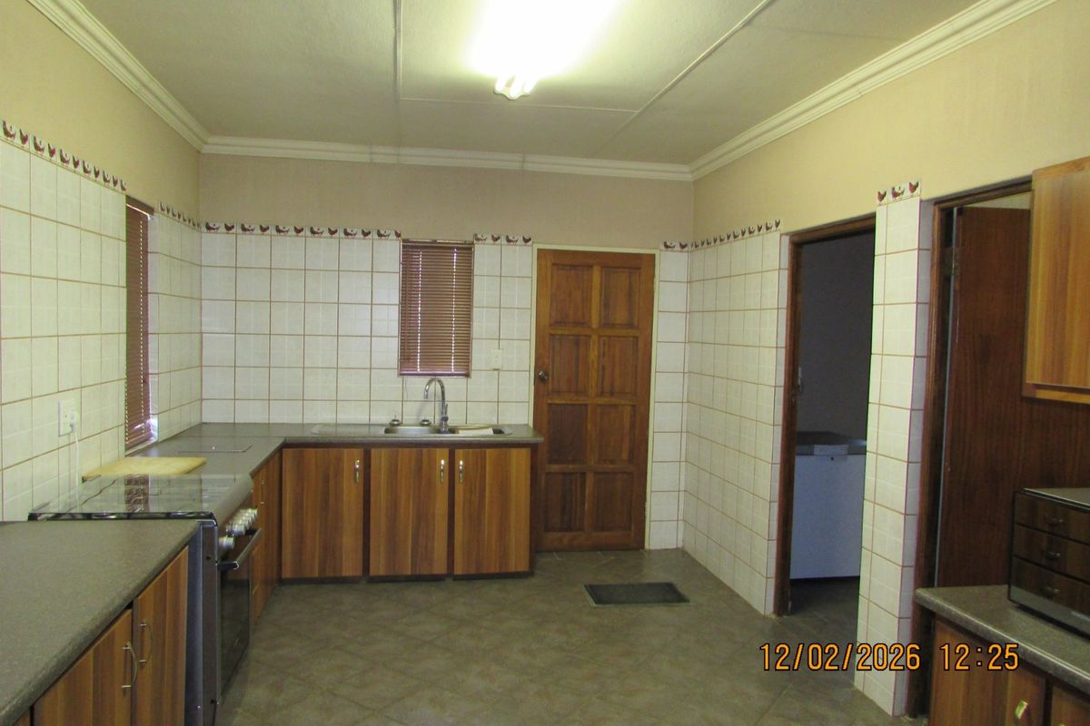 A functional kitchen featuring wood-finish cabinetry, tiled splashbacks, and a freestanding stove, offering a practical layout with direct access to adjacent utility areas.