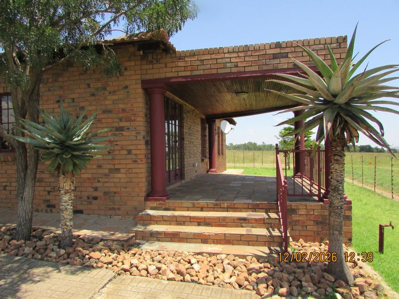 A covered face brick patio featuring tiled flooring, timber ceiling, and metal balustrades, overlooking the surrounding farm landscape.
