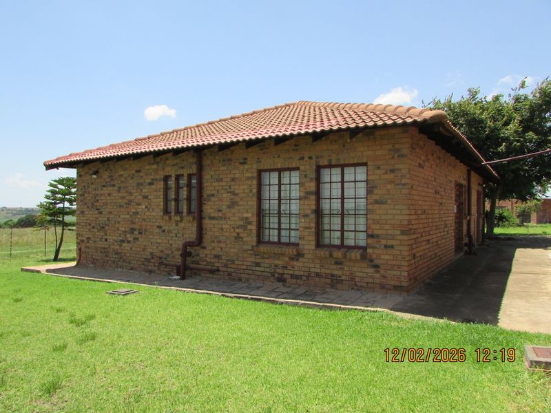 A view of the rear exterior of a face brick farm dwelling featuring a tiled roof and surrounding lawn area.