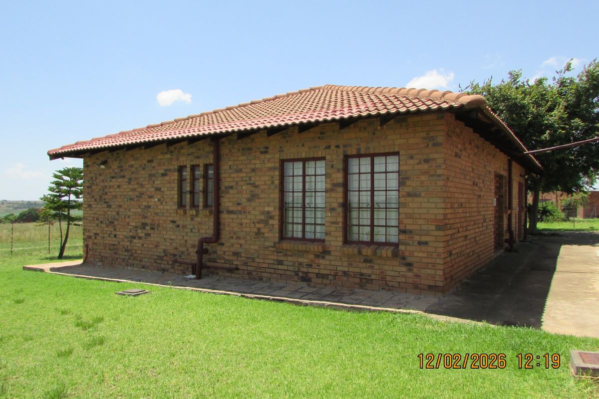 A view of the rear exterior of a face brick farm dwelling featuring a tiled roof and surrounding lawn area.