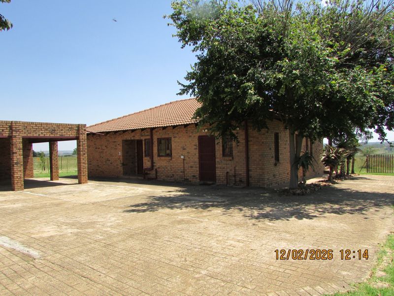 A single-story face brick farmhouse featuring a tiled roof, a covered carport, and an expansive paved driveway area.