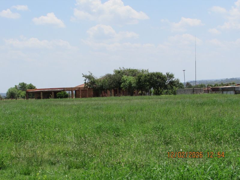A view of the rear elevation of the farm dwelling, featuring a brick structure with a covered patio area set within a large grassy field.