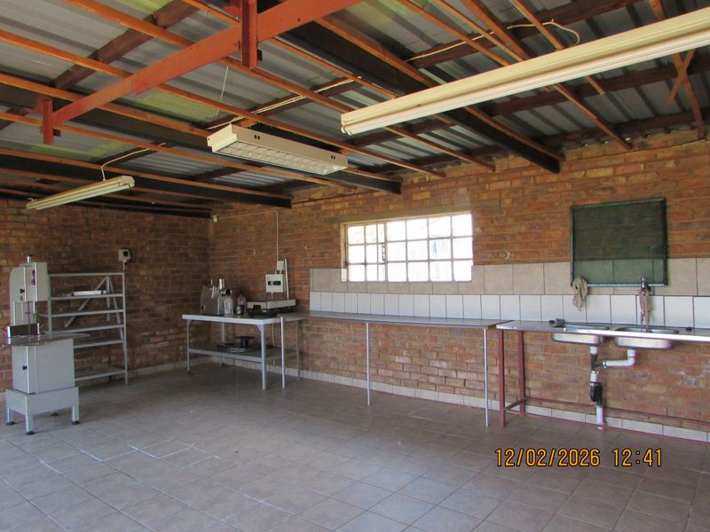 A functional utility or processing room featuring exposed brick walls, tiled flooring, a double sink, and exposed timber roof structure.