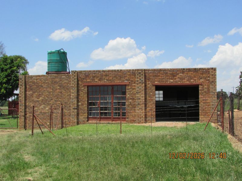 A detached face brick utility building featuring a water storage tank, sliding steel doors, and an open garage bay on a rural farm property.