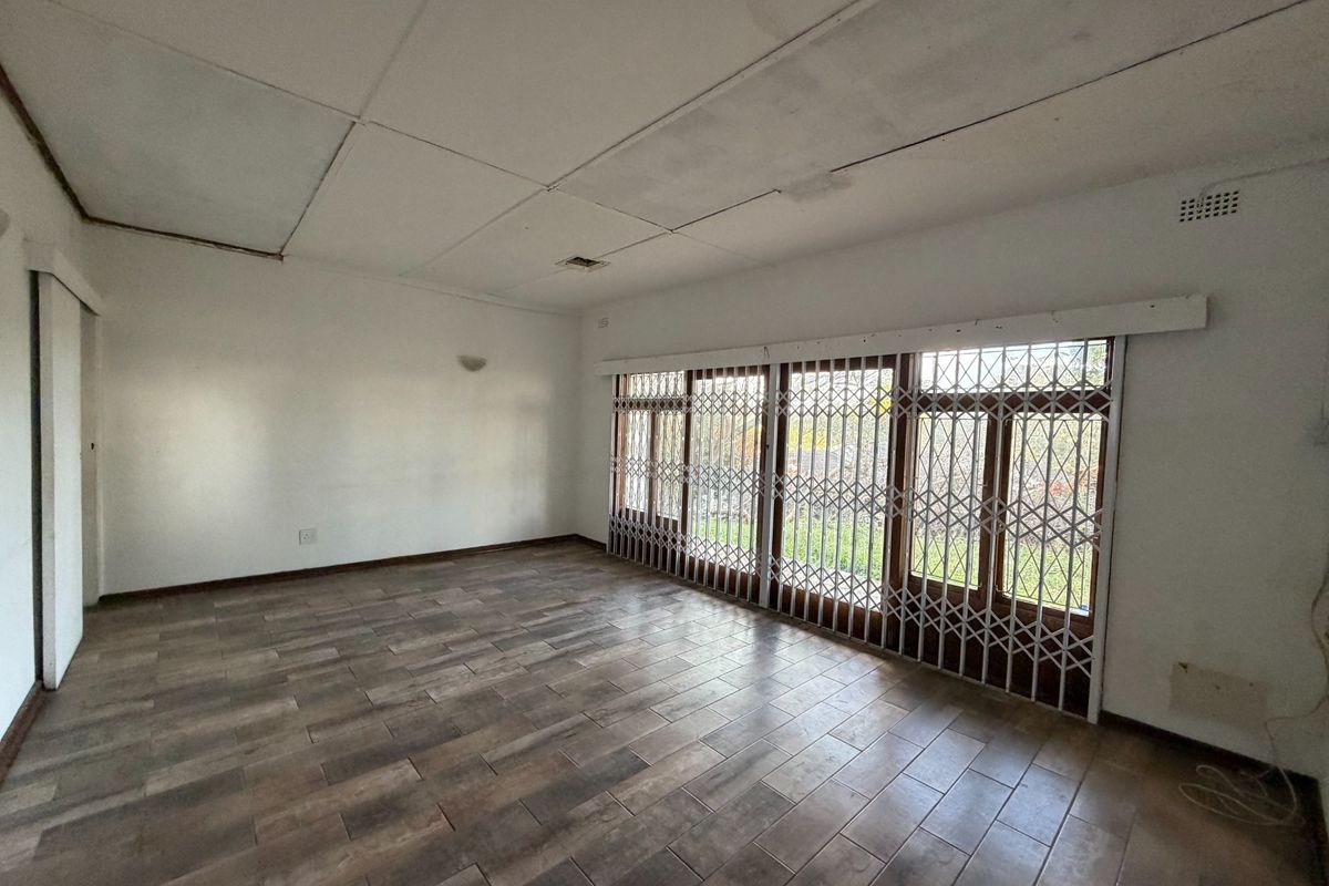 An empty living room featuring tiled flooring and a large sliding door with a security gate, showing signs of ceiling damage.