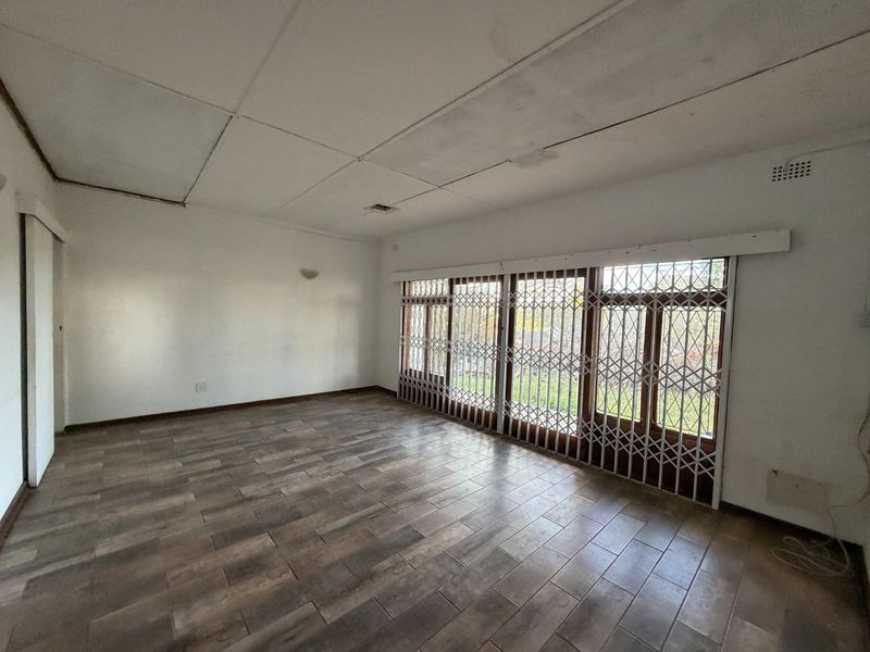 An empty living room featuring tiled flooring and a large sliding door with a security gate, showing signs of ceiling damage.