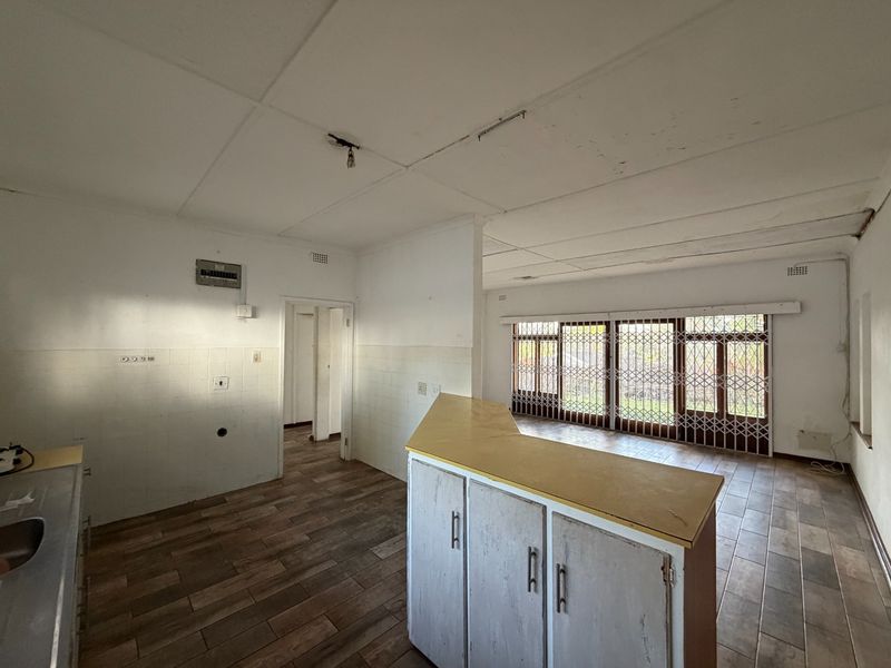 An open-plan living and kitchen area featuring tiled flooring, a breakfast counter, and security gates, currently in need of renovation and cosmetic updates.
