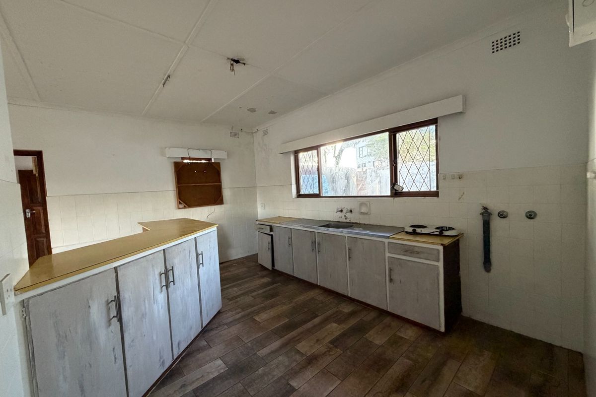 A dated, empty kitchen featuring wood-look floor tiles, built-in cabinetry, and a tiled splashback, offering a blank canvas for renovation and modernization.