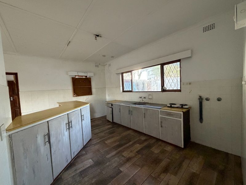 A dated, empty kitchen featuring wood-look floor tiles, built-in cabinetry, and a tiled splashback, offering a blank canvas for renovation and modernization.