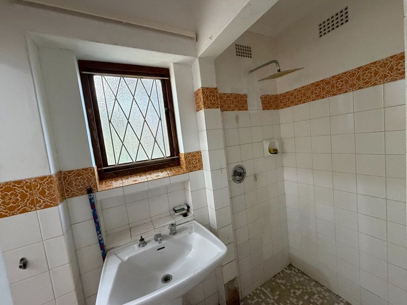 A dated bathroom featuring a pedestal basin, shower area with fixed head, and decorative tile accents, requiring modernization of finishes and fixtures.