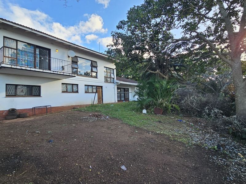 Rear view of a two-story house featuring a balcony with metal railings, security bars on windows, and an expansive, unlandscaped backyard area.