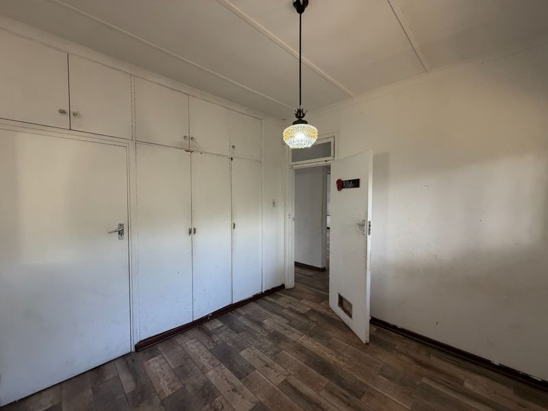 An empty bedroom featuring built-in cupboards, laminate flooring, and a central pendant light fixture, requiring cosmetic updates to the walls and doors.