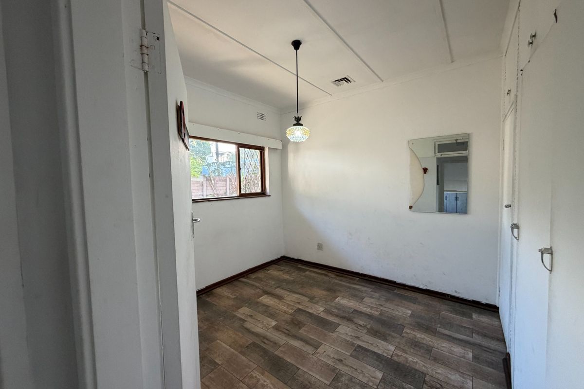 An empty bedroom featuring laminate flooring, built-in cupboards, and a pendant light fixture, ready for a fresh coat of paint and new styling.