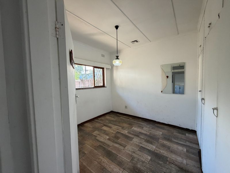 An empty bedroom featuring laminate flooring, built-in cupboards, and a pendant light fixture, ready for a fresh coat of paint and new styling.