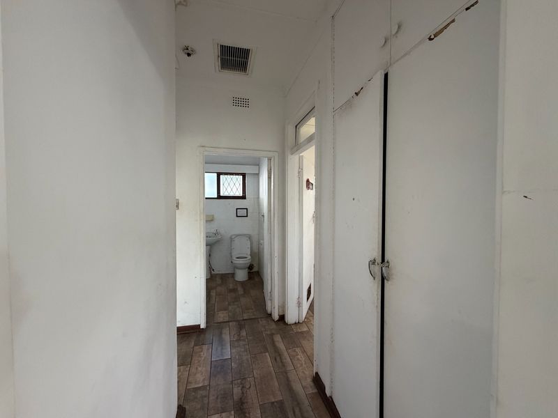 A narrow hallway featuring tiled flooring and built-in storage cupboards, leading towards a bathroom area.