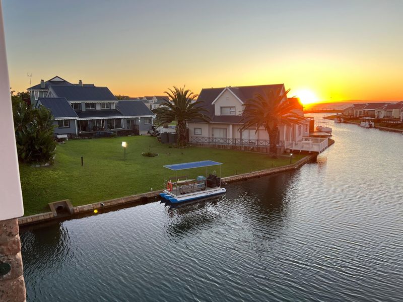 A scenic sunset view overlooking a canal-front property with a private garden, jetty, and waterfront access.