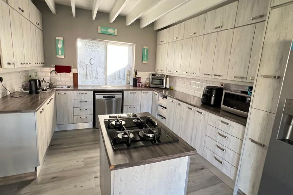 Modern kitchen featuring a central island with gas hob, extensive light wood-grain cabinetry, subway tile backsplash, and exposed beam ceiling.