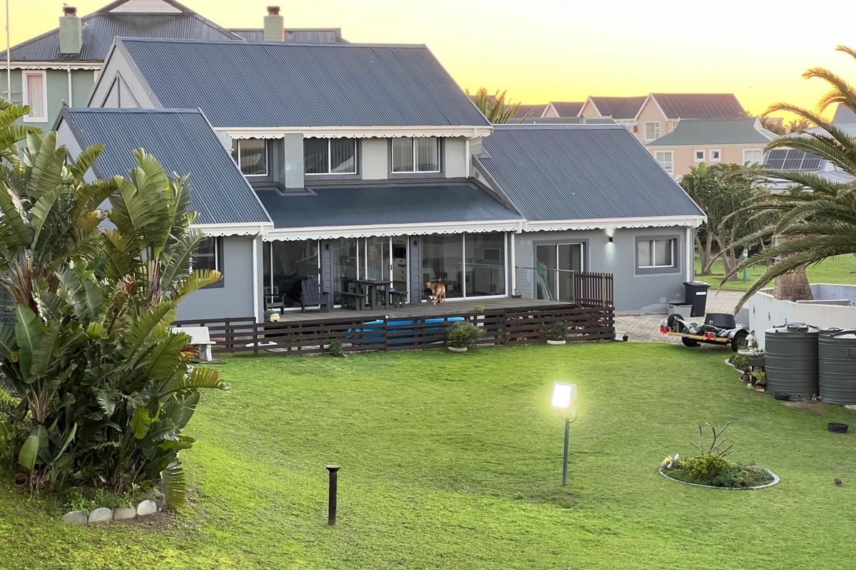 Rear view of a two-story house featuring a large lawn, a spacious timber deck, and sliding glass doors leading into the living area.