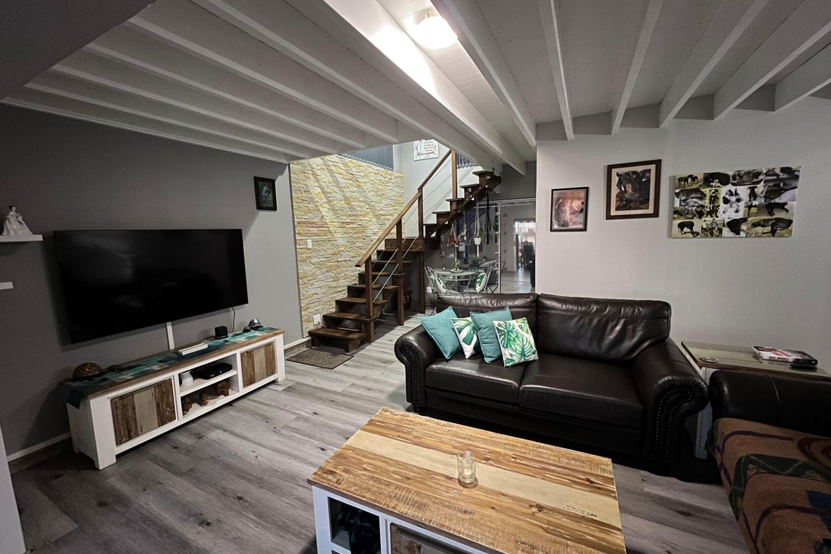 A comfortable living room featuring a striking stone accent wall, a timber staircase, exposed beam ceilings, and modern laminate flooring.